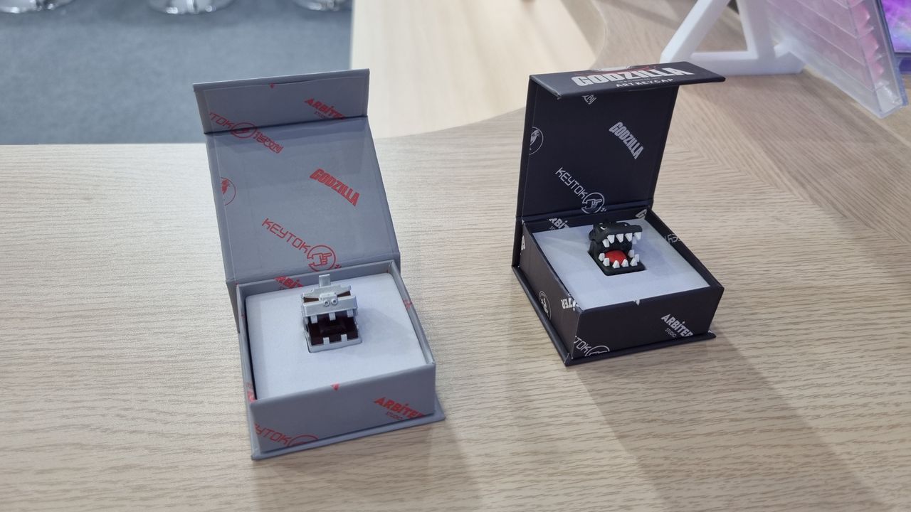 Two Godzilla keycaps in boxes on a table