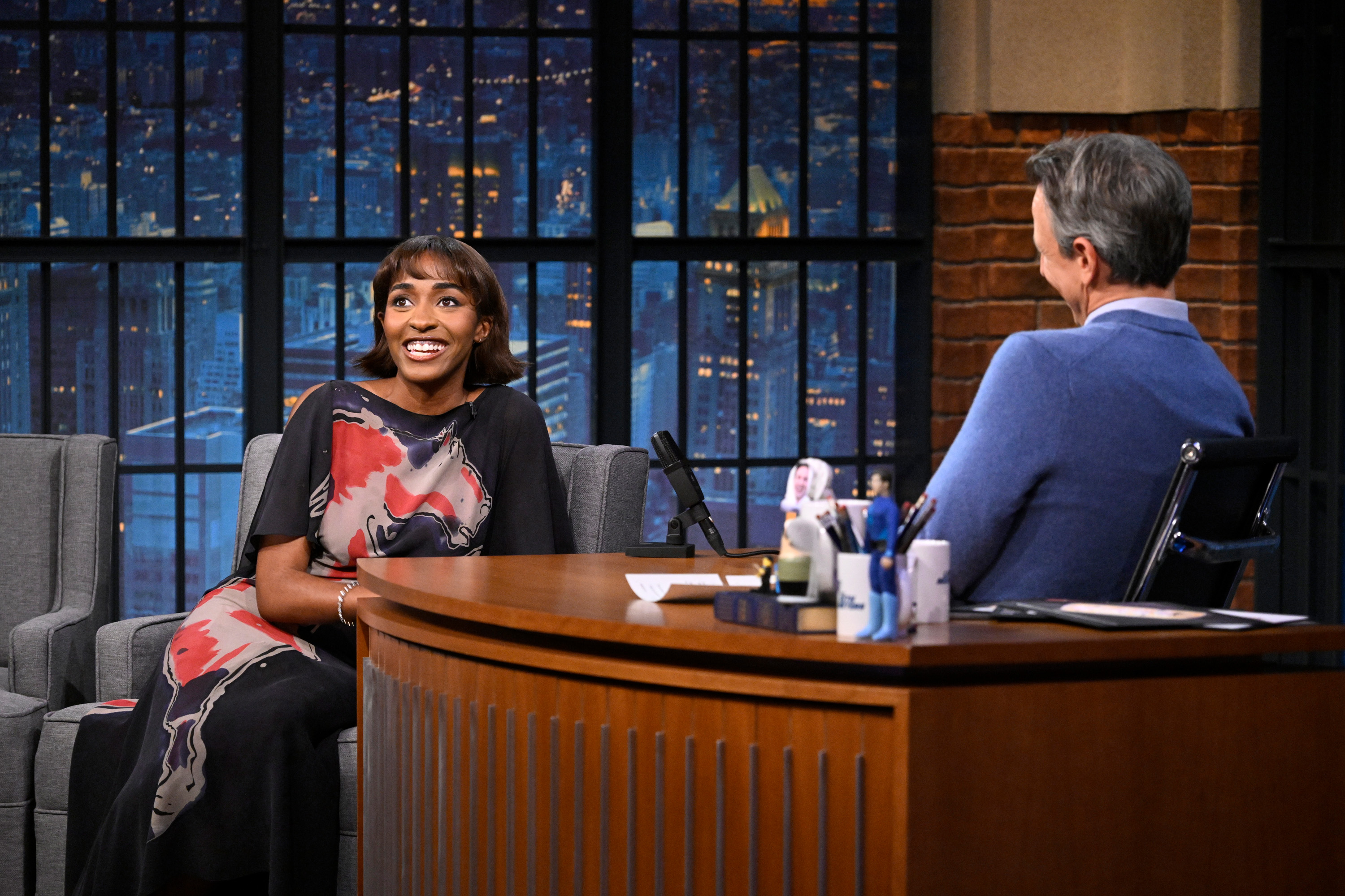 a black woman with short, brown hair being interviewed by a white male on a talk show set