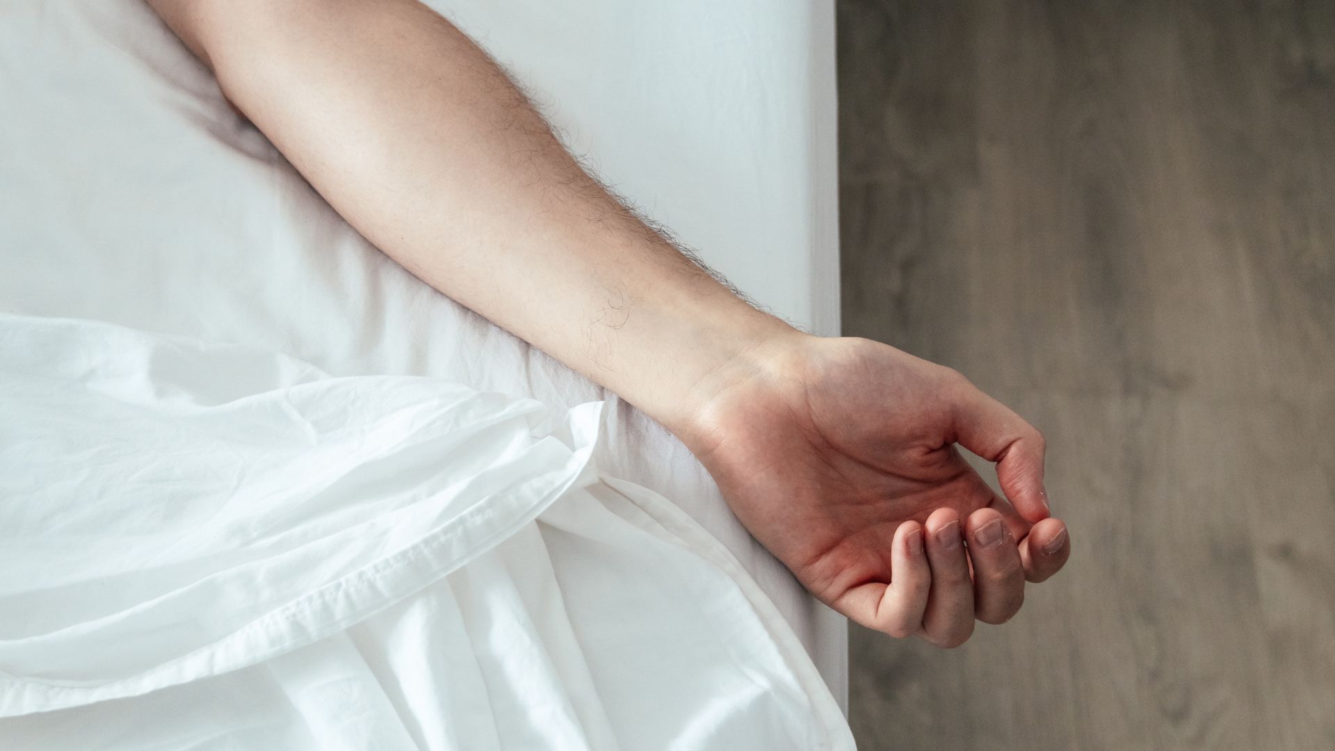 A man's arm is relaxed against white bedsheets, indicating he's sleeping well.