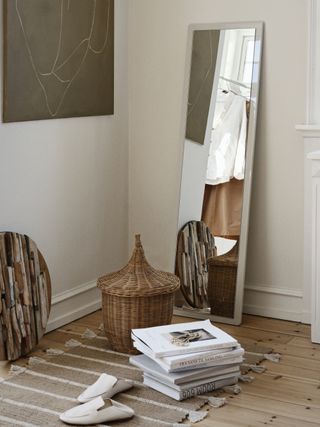 A corner of a room with a mirror, slipped off shoes , a pile of books and a basket of the floor