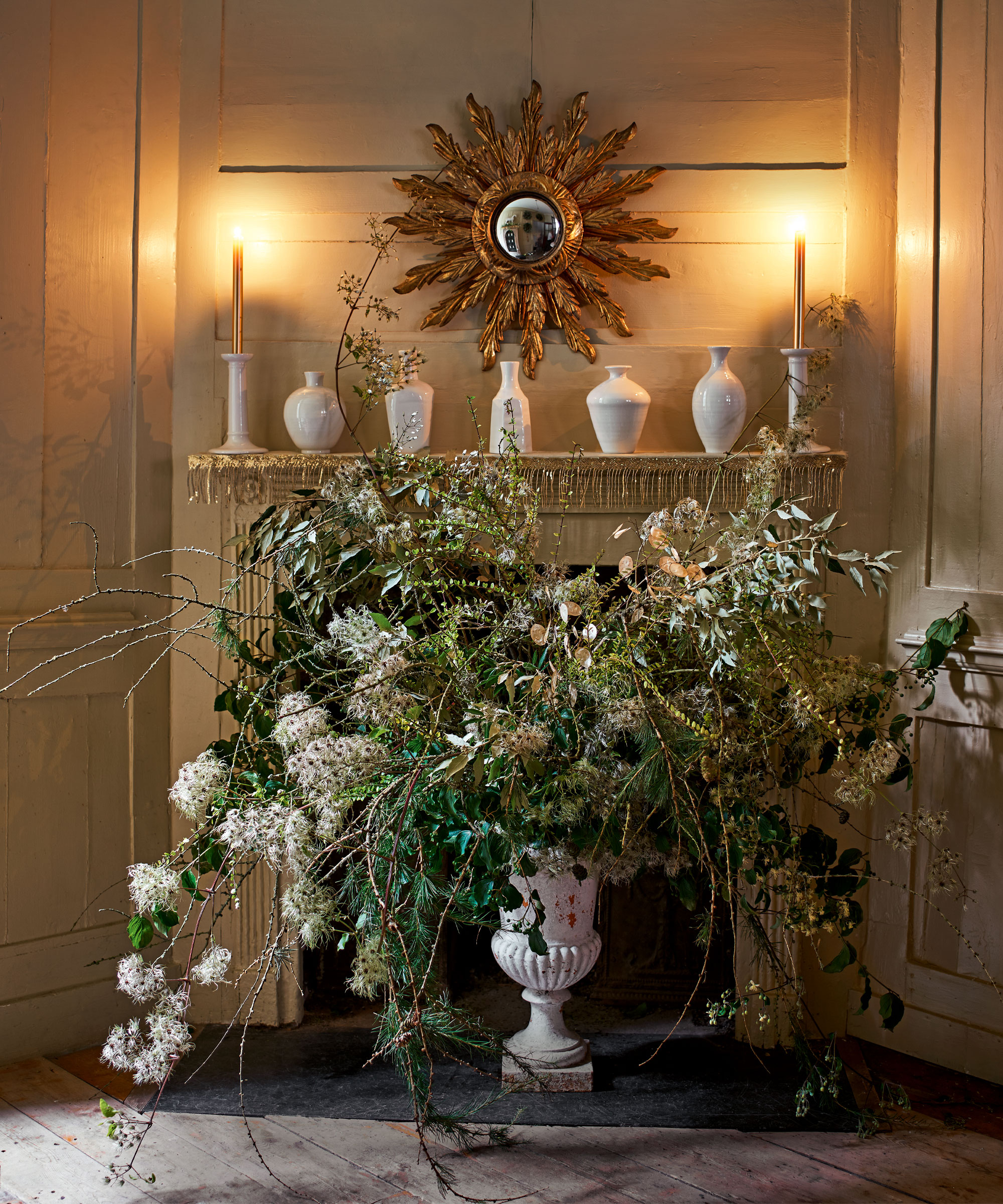 Fireplace decorated with candles, ceramics and vase of flowers and foliage