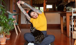 Tattooed woman stretching at home with cat in lap