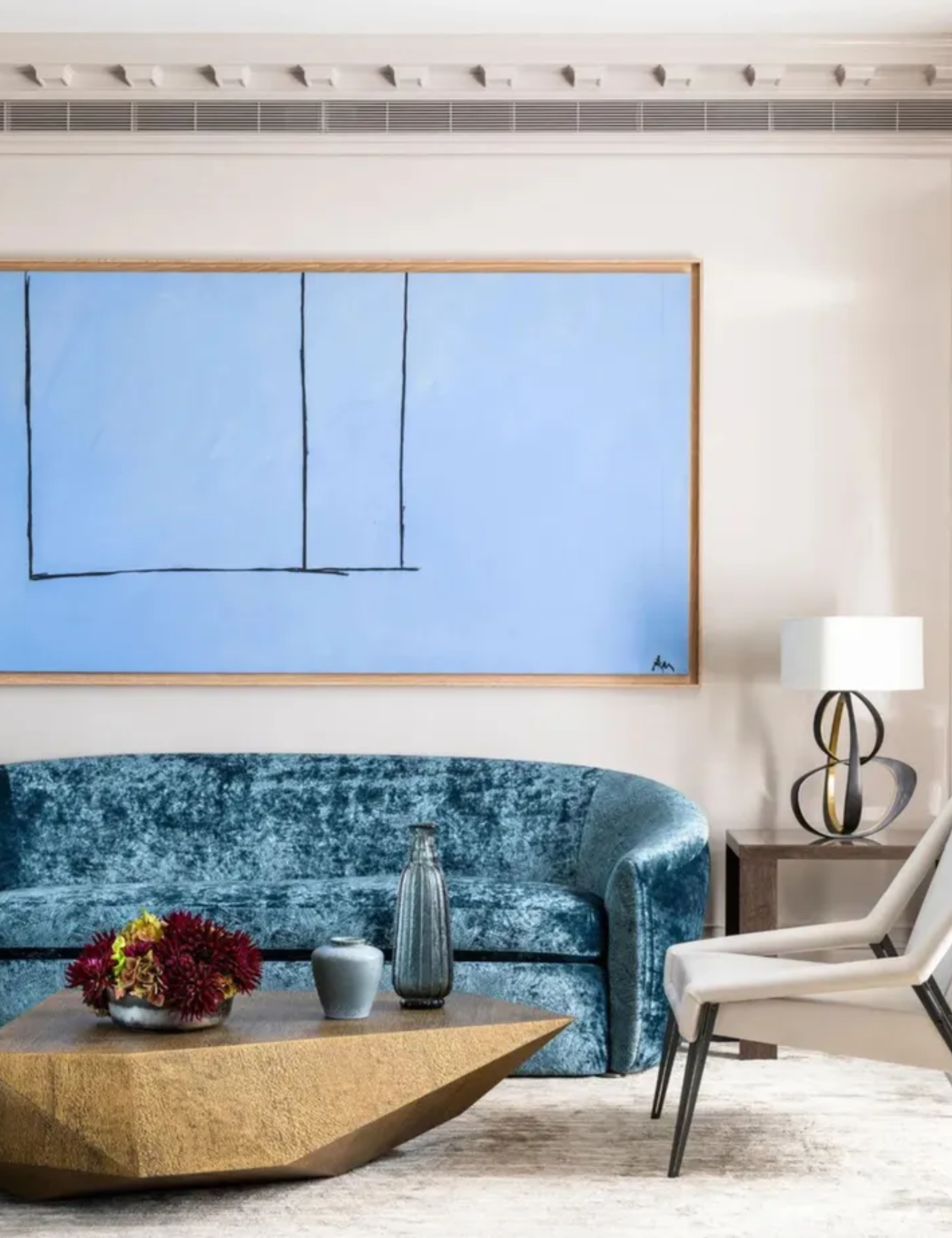 Modern cream living room with a curved crushed velvet sofa and a large blue artwork above
