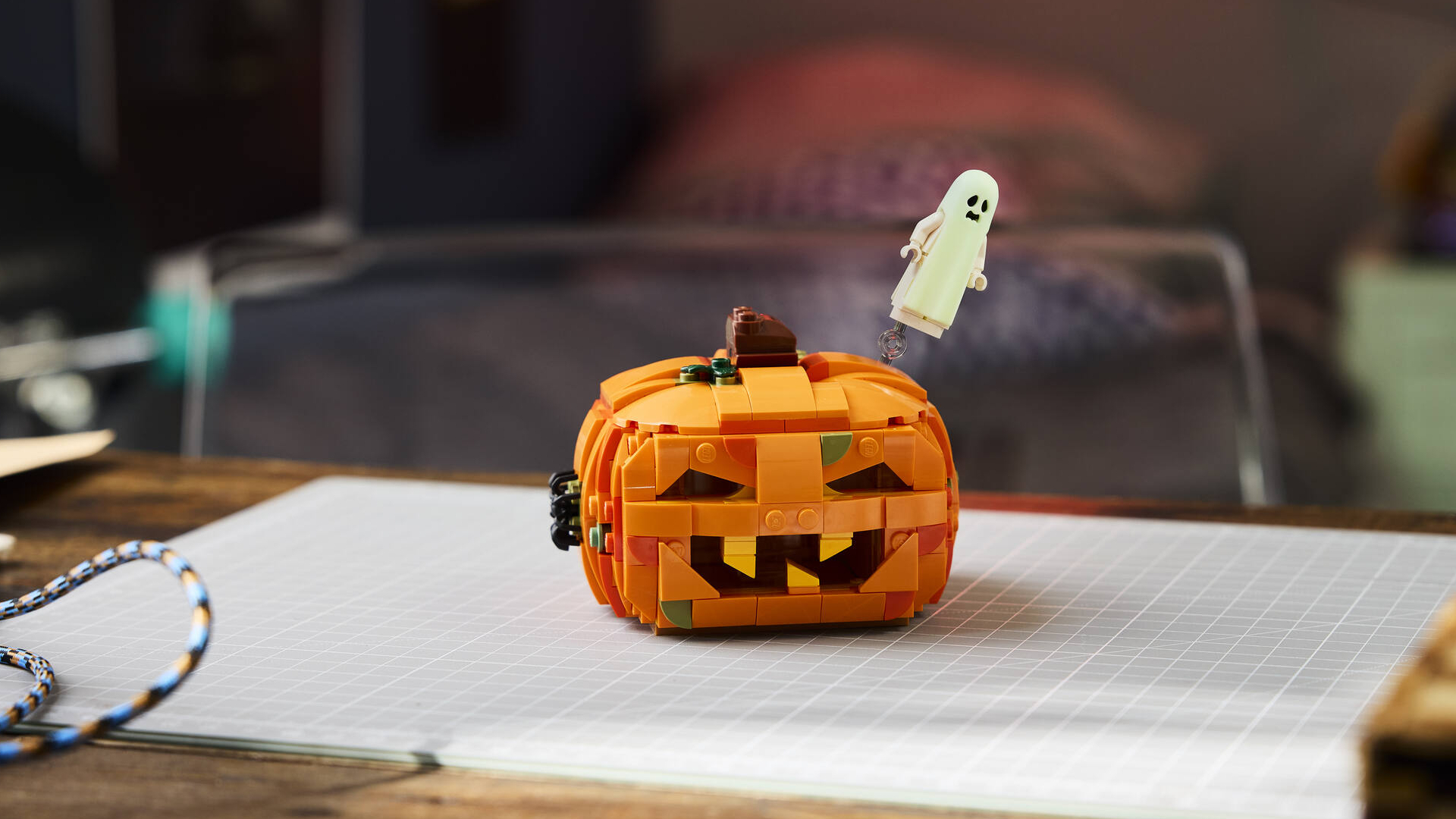 A Lego Pumpkin with floating ghost on a table with a gridded piece of paper