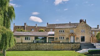 stone cottage with a side extension featuring a glazed link and modern sliding glass doors. Patio with a stone retaining wall and steps leading down to a lawned garden area