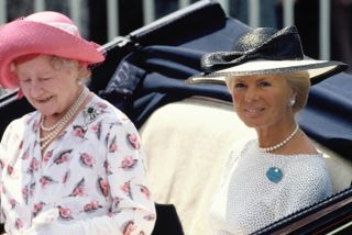 The Queen Mother wearing a white floral dress with a pink hat riding in a carriage with the Duchess of Kent, wearing a black hat and pearls