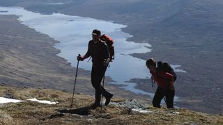 Two people hiking up a munro using trekking poles