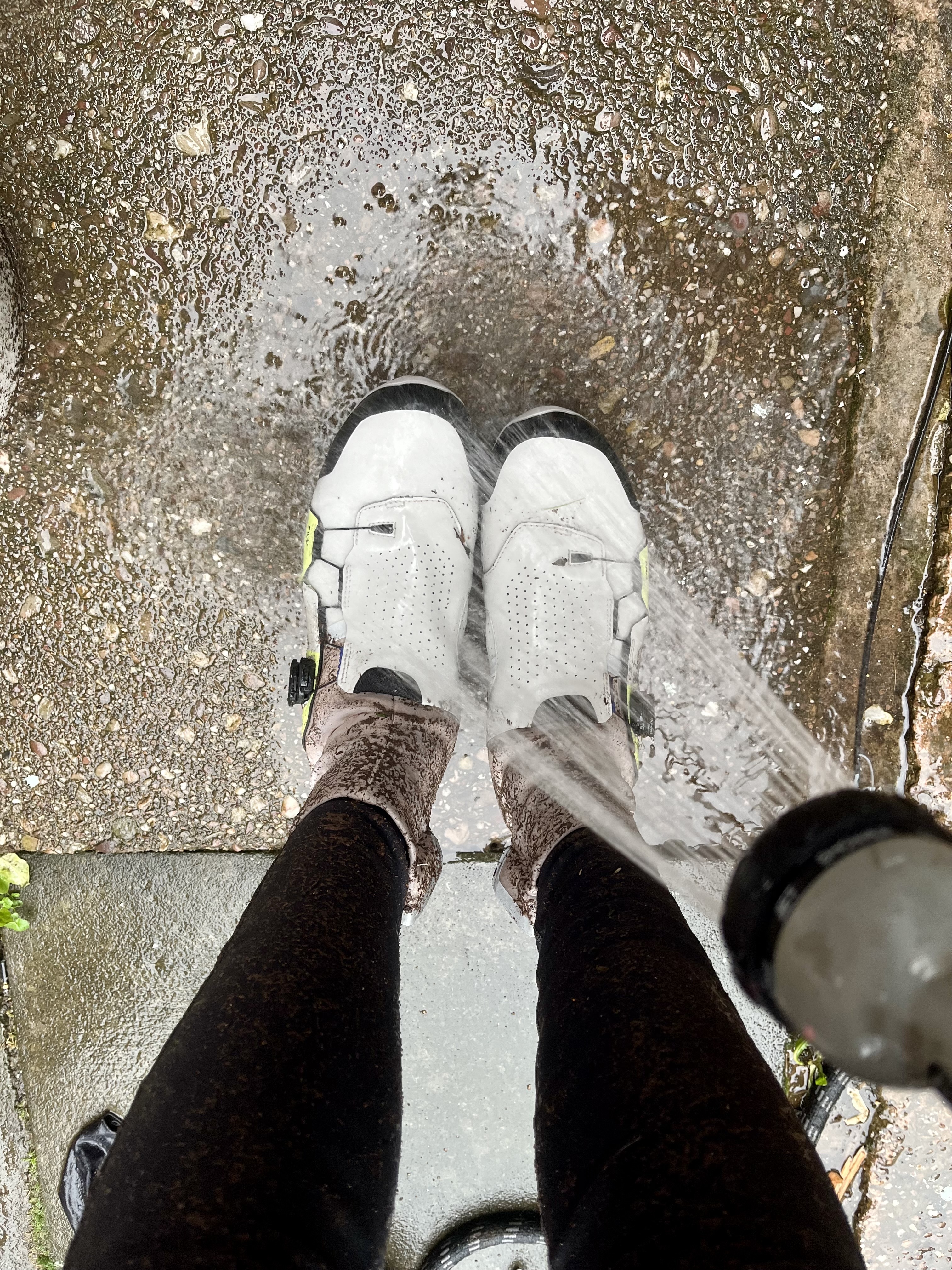 A cyclist cleaning winter cycling shoes with a garden hose