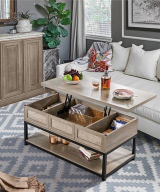 Extended lift top coffee table open geo pattern rug, with lower shelf, open mid section with compartments, and top tier with fruit bowl and drink bottle.