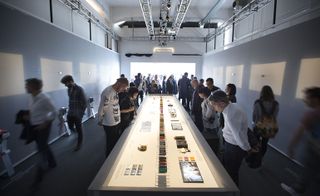 View of Hyundai's interactive exhibition featuring a long illuminated display table with various items on show. Multiple people can also be seen