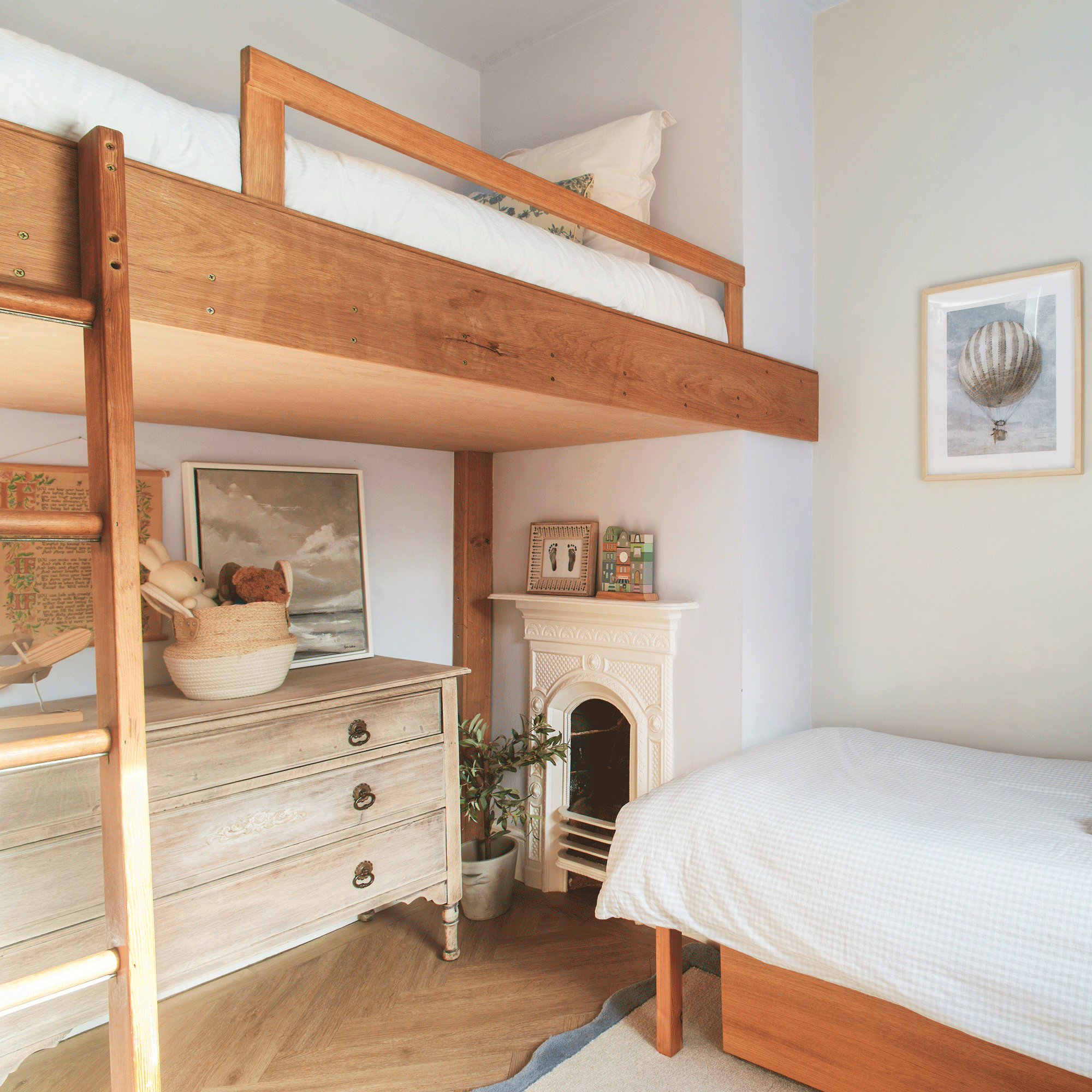 a child's twin bedroom with a loft bed and a single bed, a chest of drawers and several artworks
