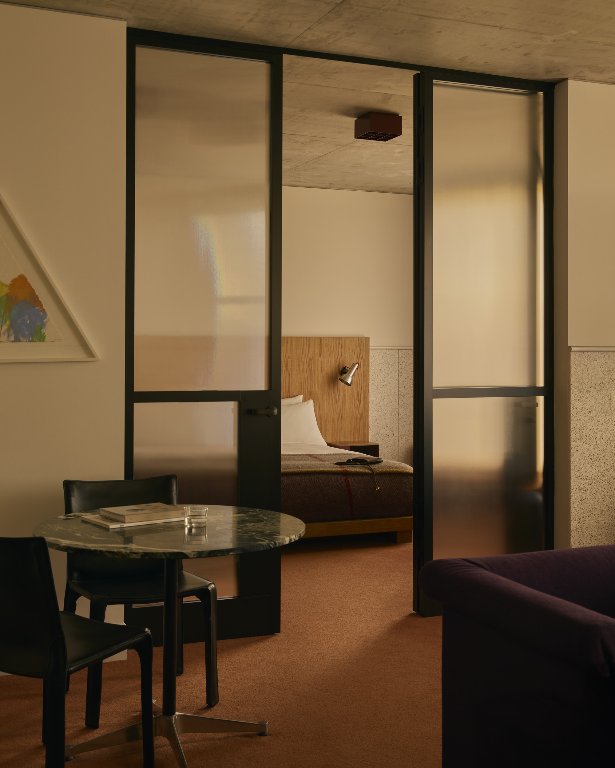 a hotel suite with a terracotta color carpet and a glass room divider between the bedroom