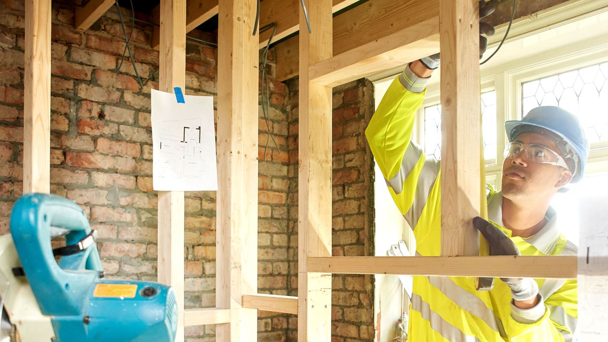 Man measuring timber stud work inside house