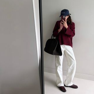 Woman wears burgundy jumper, white jeans, brown loafers