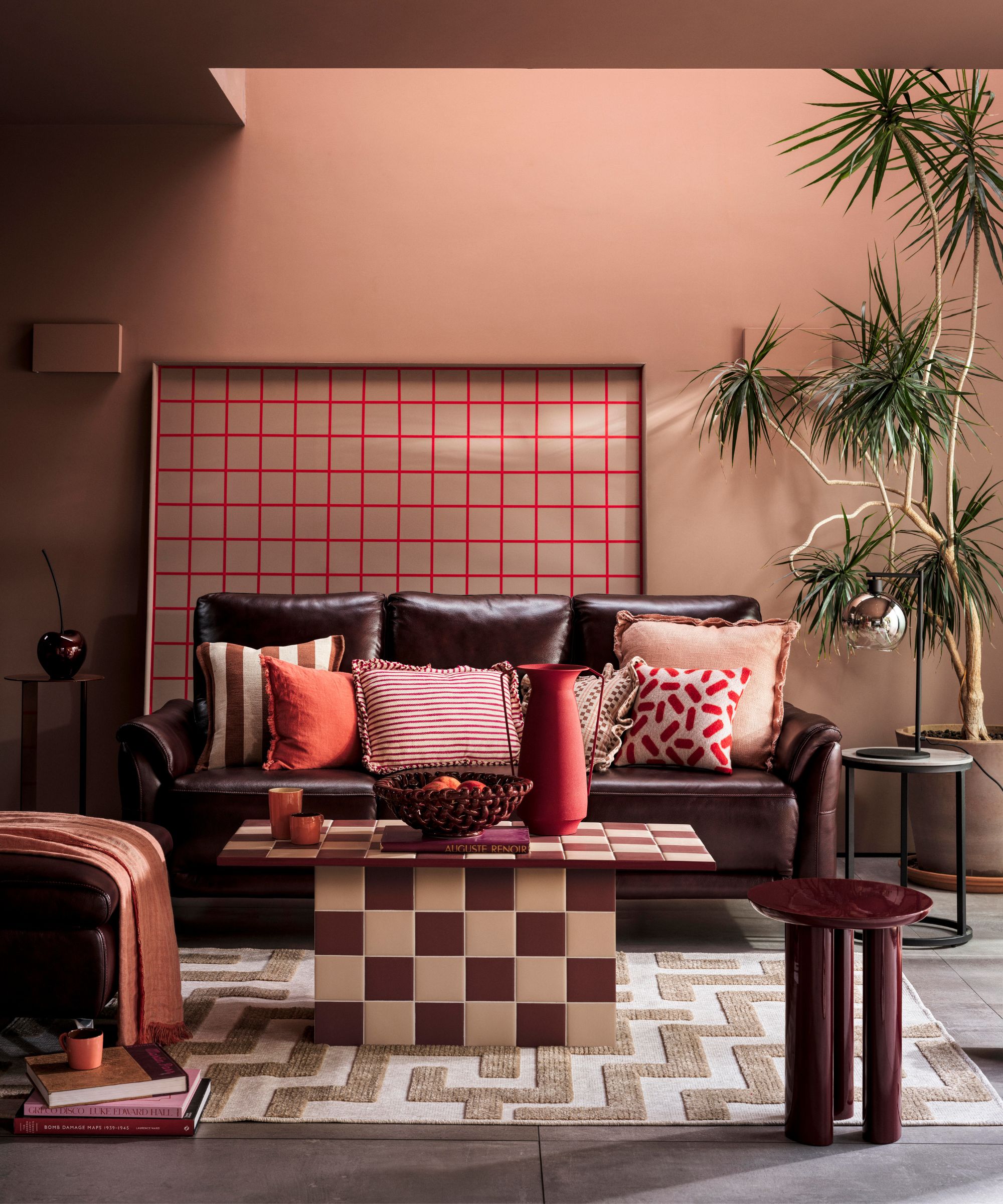 dusty pink living room with a dark burgundy leather couch, pink striped and red ruffled pillows with a pink and burgundy checkerboard tiled coffee table