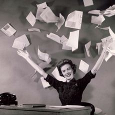 Woman at desk topping papers in air