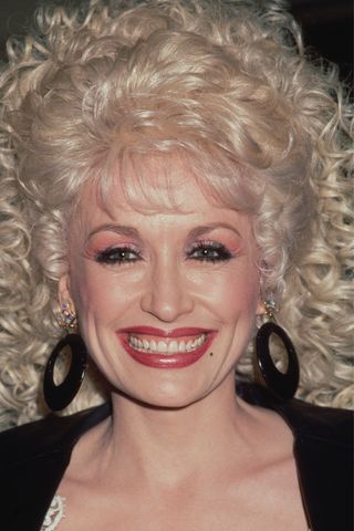 Dolly Parton pictured with bold eyeliner, pink eyeshadow and pink/red lipstick