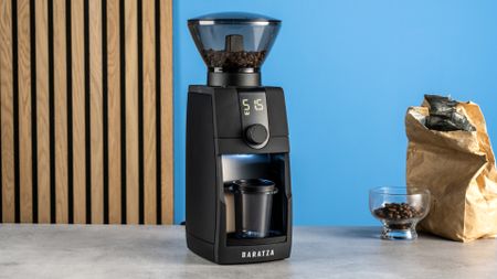 the baratza encore esp pro coffee grinder photographed against a blue tom's guide background with a bag of coffee to the side and showing the grinder in action