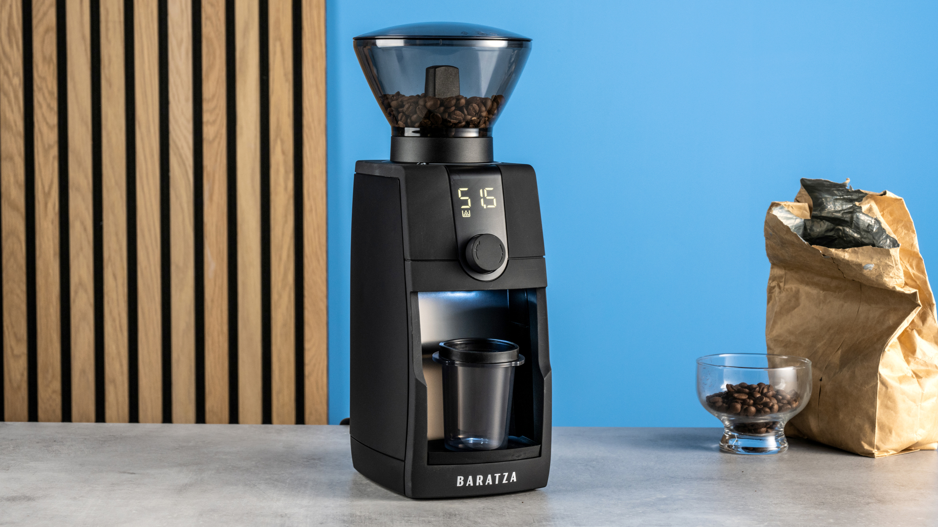 the baratza encore esp pro coffee grinder photographed against a blue tom's guide background with a bag of coffee to the side and showing the grinder in action