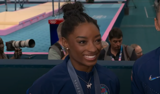 Simone Biles smiling with a gold medal around her neck at the Paris games.