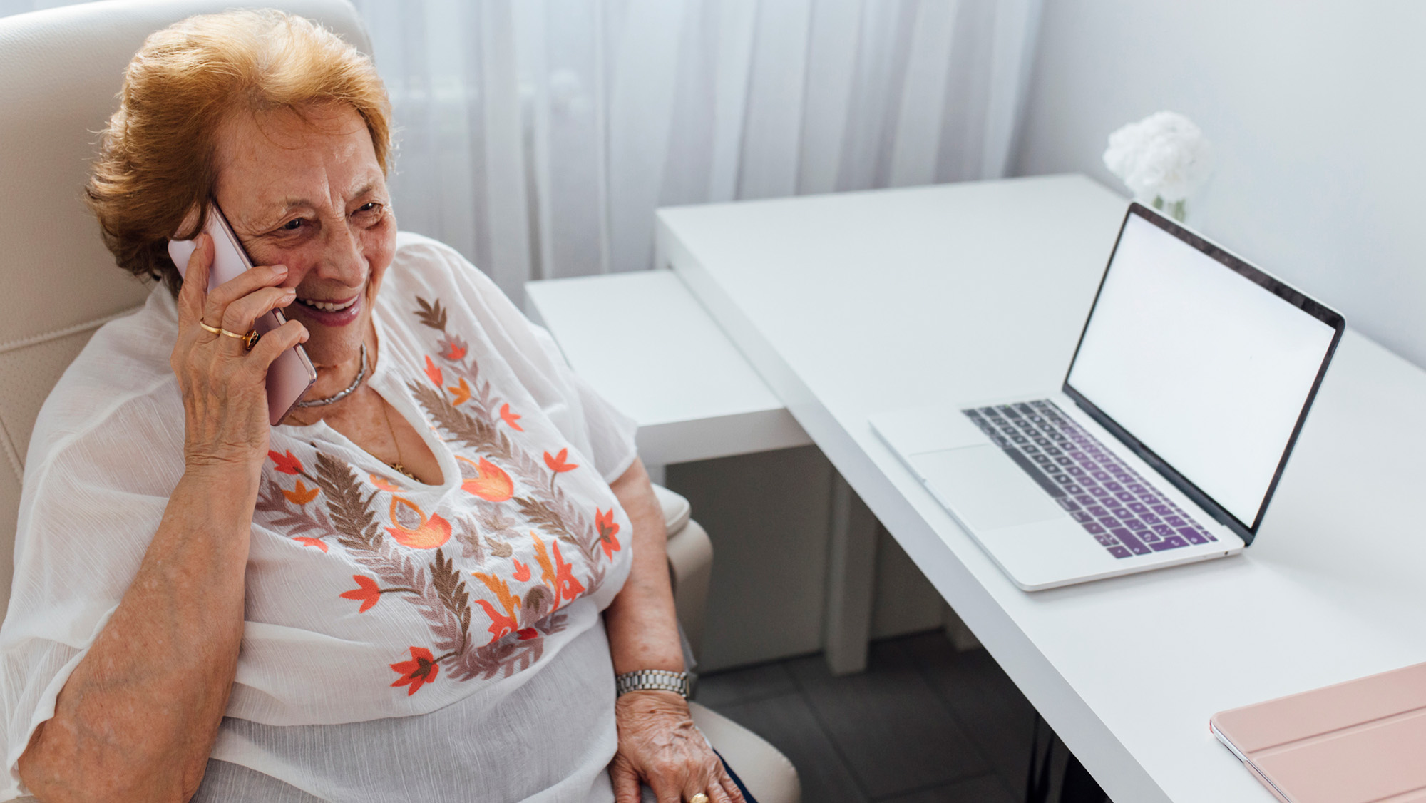An older woman with red hair sits behind a desk and talks on the phone.