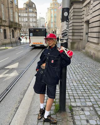 Influencer @sofiamcoelho wears a pair of leopard print trainers with denim shorts, a denim jacket, and red accessories whilst standing on the pavement