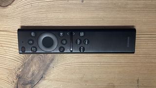 En svart fjärrkontroll till Samsung QN95B QLED TV som ligger på ett träbord.