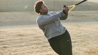 TRX Home2 System suspension trainer review: A woman in a grey workout sweater trains her upper body outside
