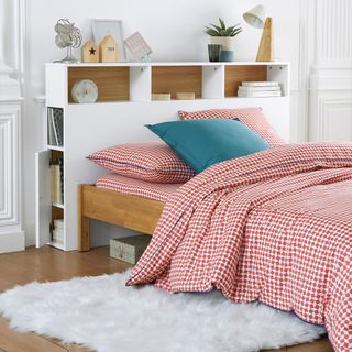 A white storage bed by Le Redoute with shelving incorporated into headboard. Bed linen is red chequered and teal statement pillow
