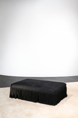 A rectangular black foot stool with tassels on the sides.