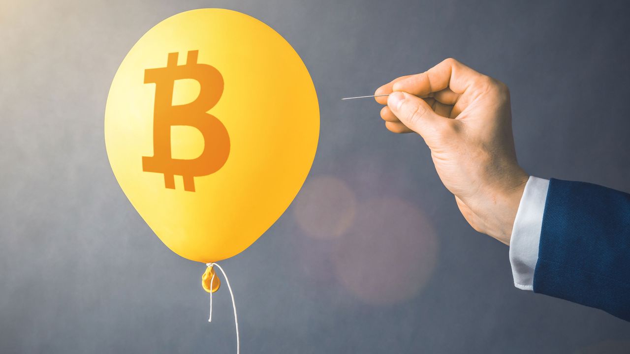 A balloon with a bitcoin symbol on it is in danger of being popped with a needle.