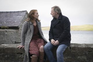 Lucianne McEvoy as Meg and Douglas Henshall as Perez in the season 7 finale of Shetland. Meg and Perez are both sitting on a low wall, facing each other, having a heart-to-heart, with the sea behind them in the background