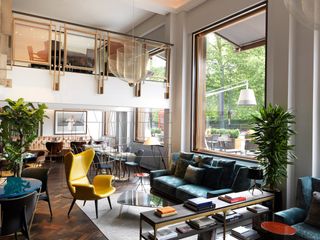 A mid-century modern-meets-modern glamour hotel lobby features strikingly colorful, geometrical furniture, plants, books, and huge windows.