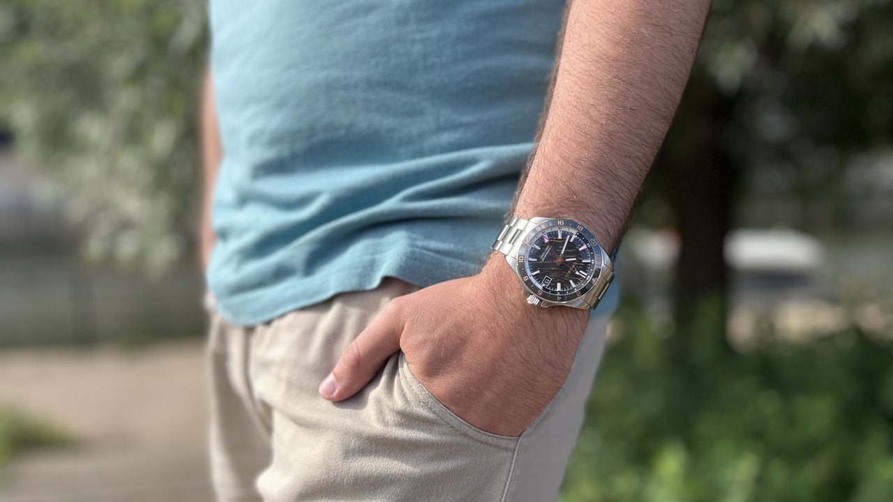 The Norqain Neverest Glacier GMT worn on a wrist against a green background