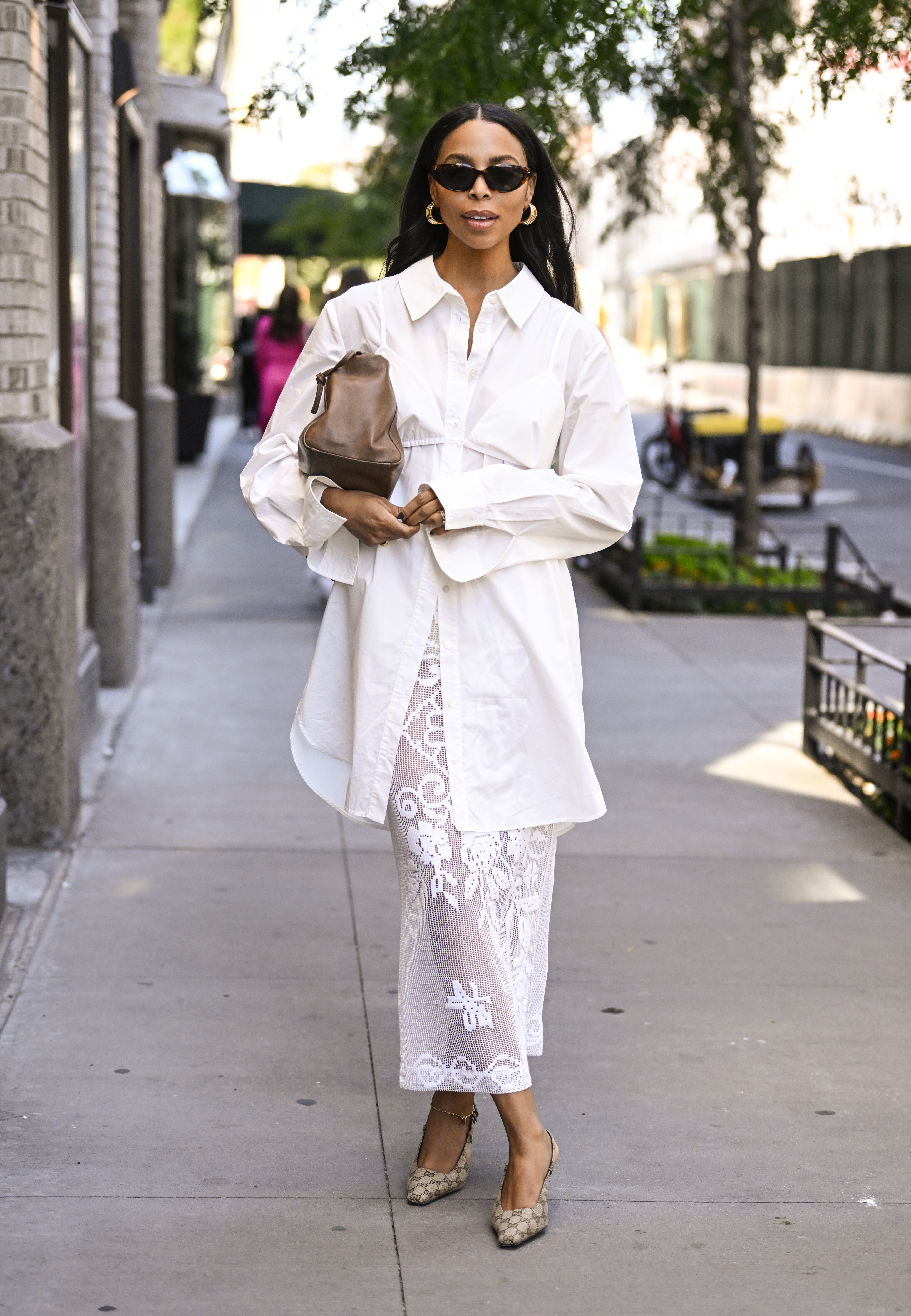 Janelle Lloyd is seen wearing a white oversized shirt, laced white skirt and brown bag with black sunglasses outside the Patbo show during NYFW Spring/Summer 2025