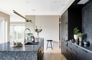 A kitchen with wooden flooring, black cabinetry and a large island