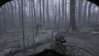 A first-person perspective of a soldier carrying a gun making his way through a grey, foreboding forest of dead trees.