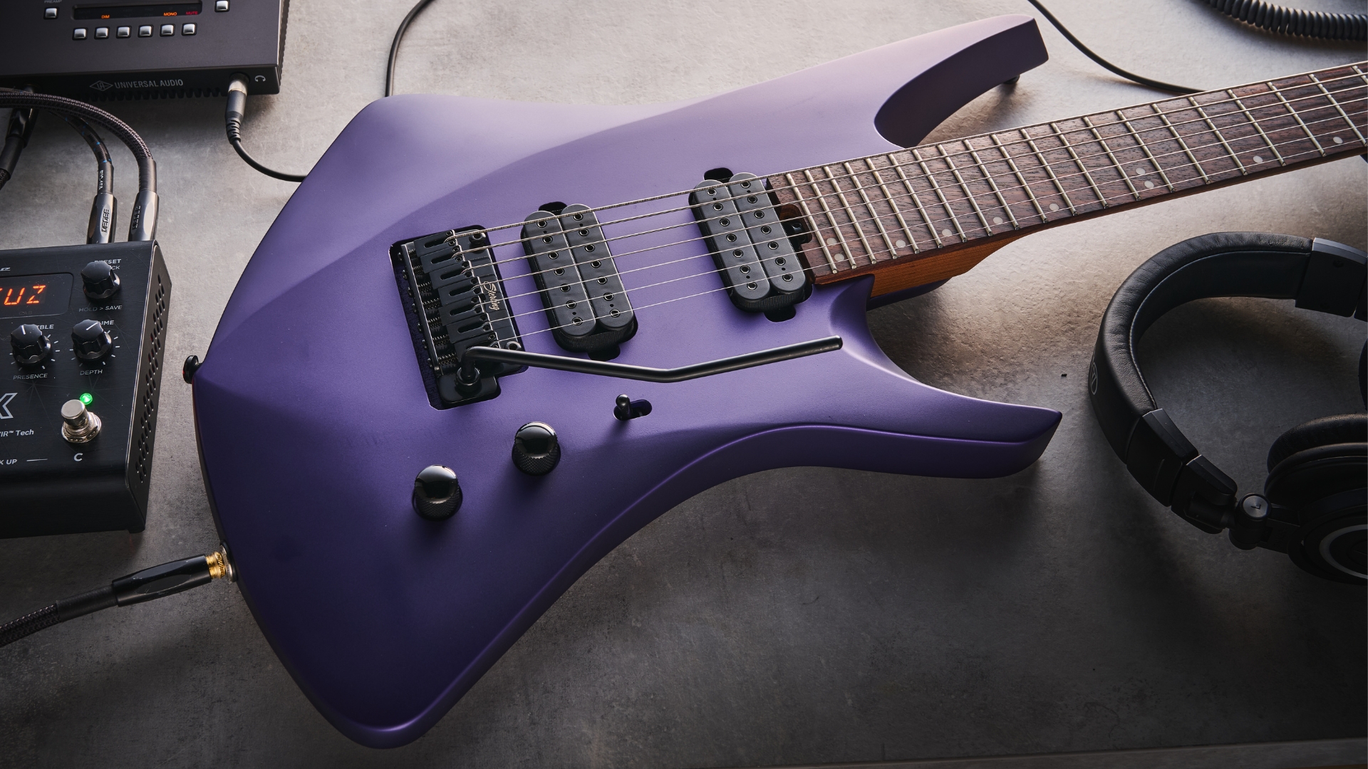 A Sterling by Music Man Kaizen 7 on a desk with various bits of music making gear in the background