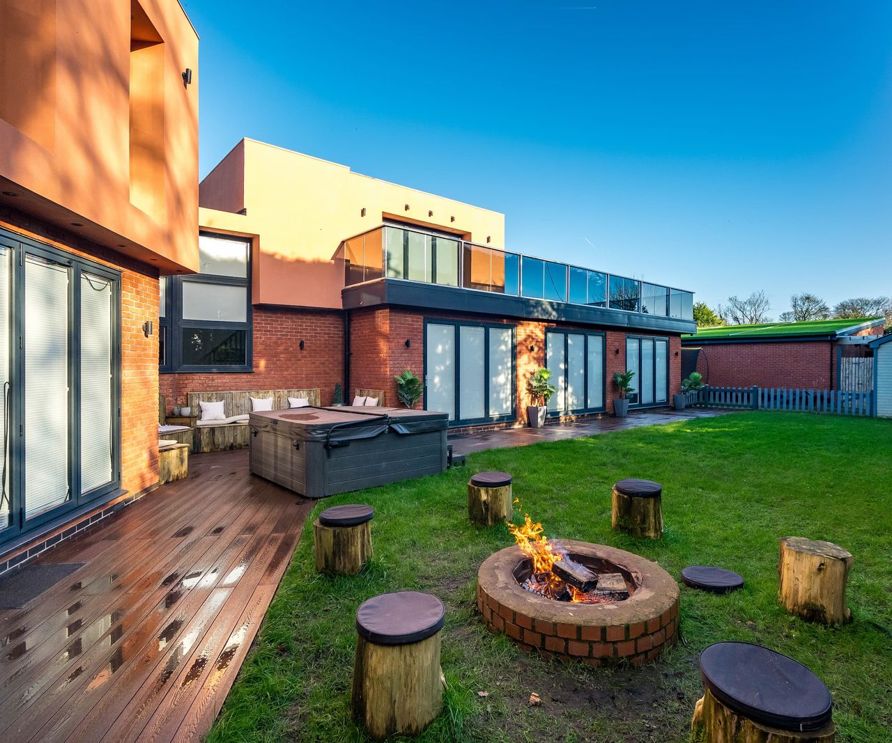 A garden with a firepit and logs to sit on with a hot tub overlooked by a balcony
