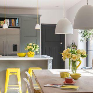 A neutral kitchen diner with a white island, yellow bar stools and pendant lights