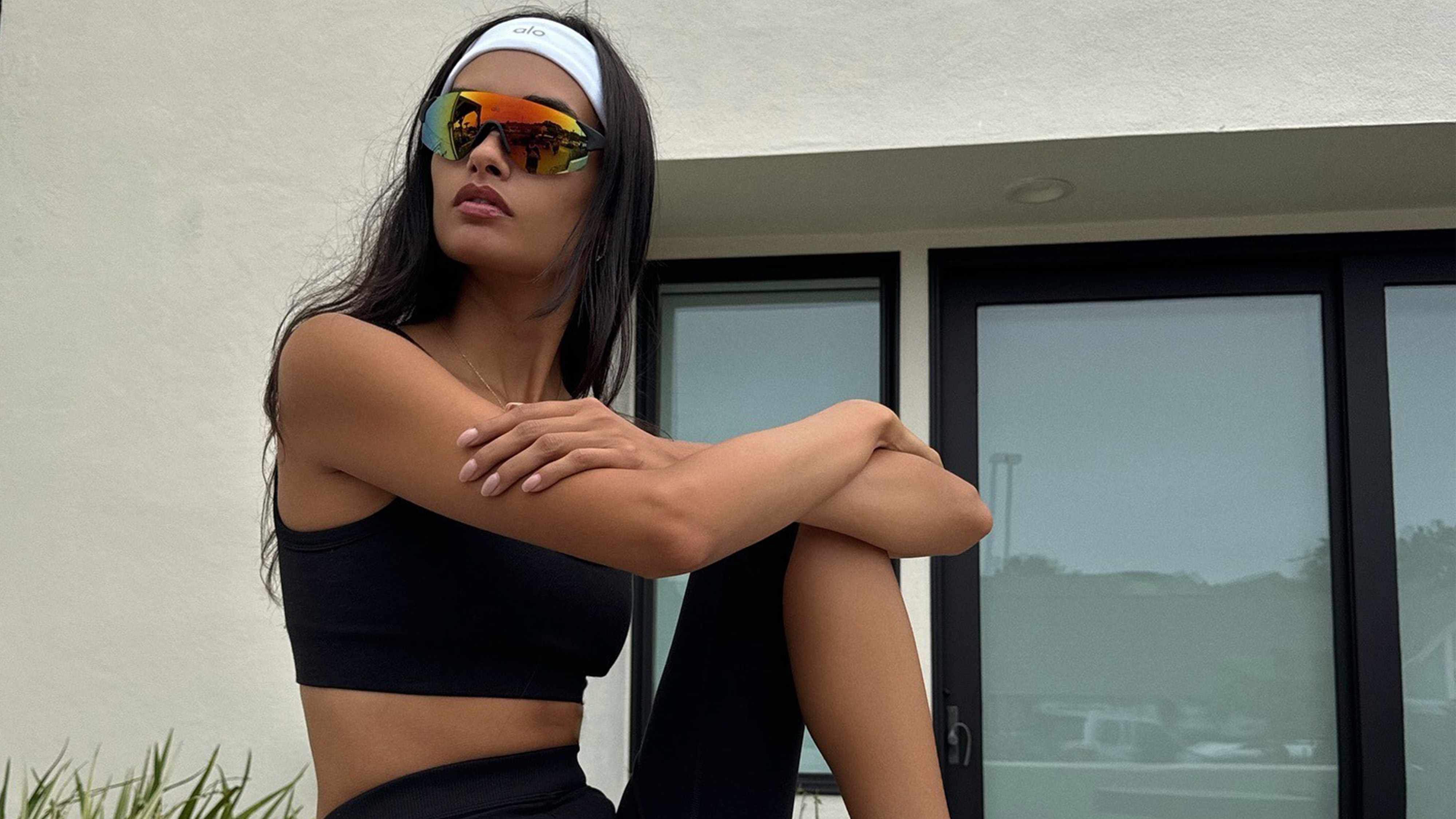 Gizele wears a white headband, black sports bra and colored sunglasses.