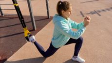 Woman performs a single-leg exercise using a TRX suspension trainer outside