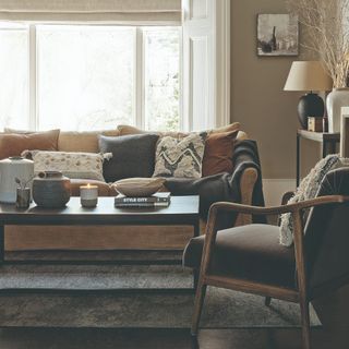 A living room with a light brown sofa and a dark brown accent chair decorated with textured cushions