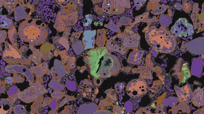 A microscope image of lithified slag. We see purple and light orange blobs with blue and green inclusions.