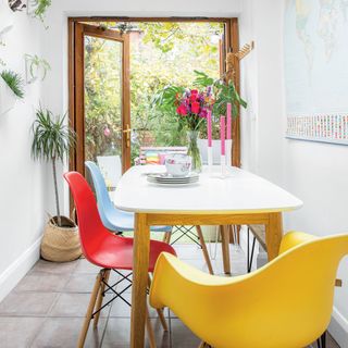 White extended dining area with tiled flooring, patio doors, wall planters, a white dining table and colourful mid-century chairs