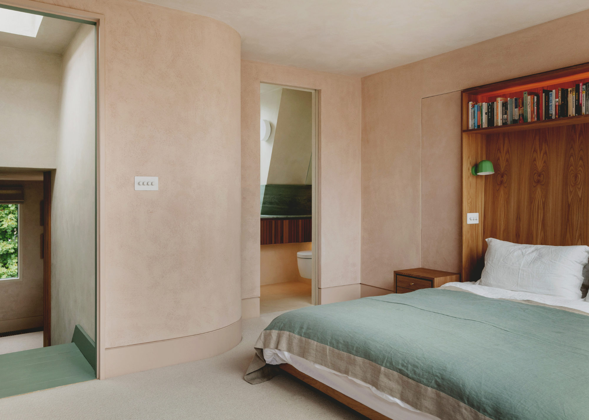 Curved walls in a loft bedroom with pink plaster paint, wooden bed and sage green features