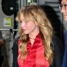 Jennifer Lawrence wears a black lace skirt with a red silk shirt and flat pumps