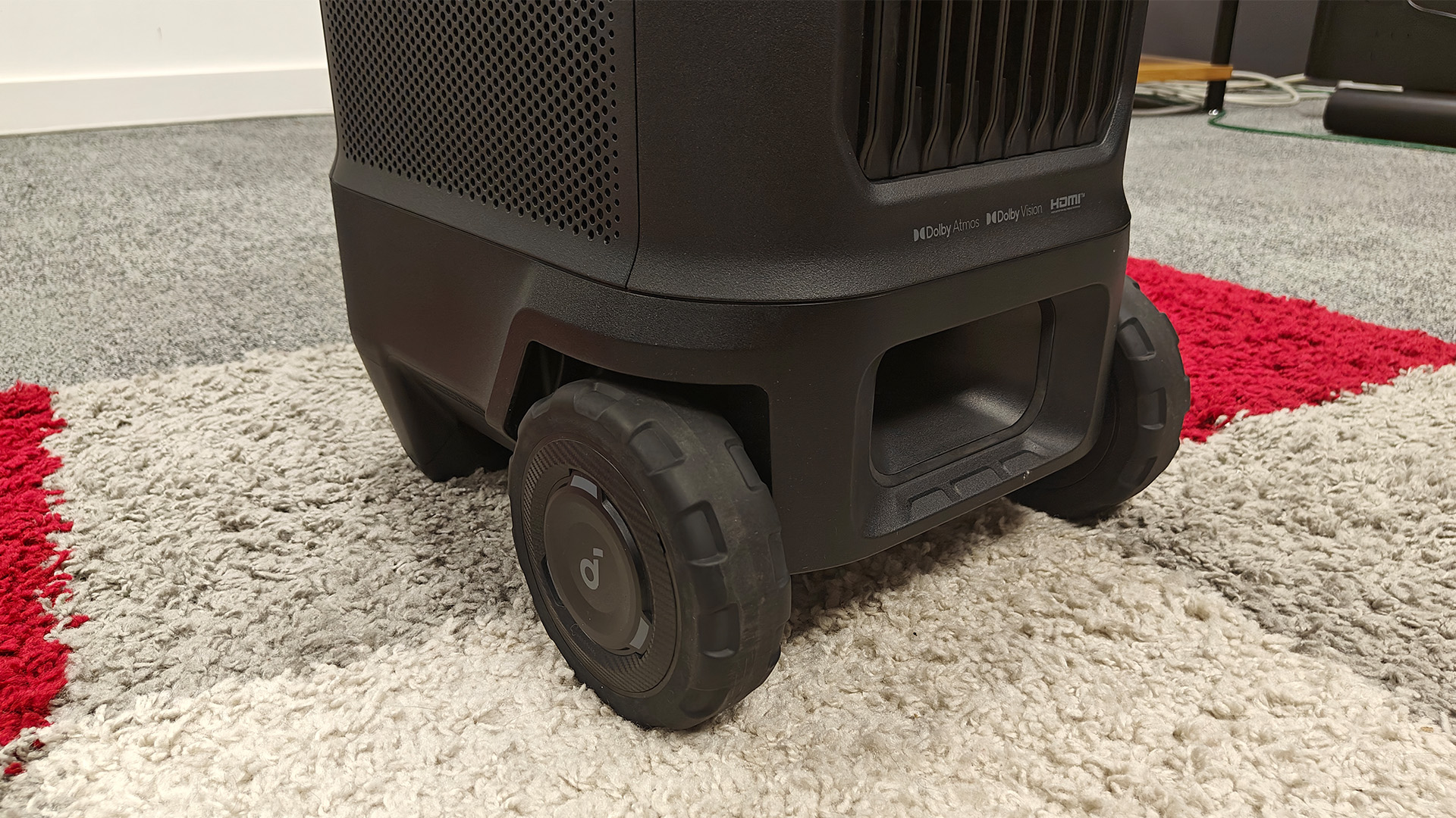 Soundcore Nebula X1 Pro home cinema projector showing wheels on red, grey and white rug