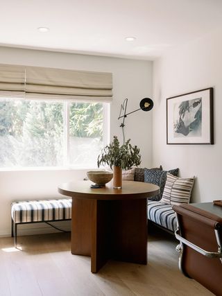 A light entryway with table in center topped with plant and surrounded by bench covered in striped neutral cushions.