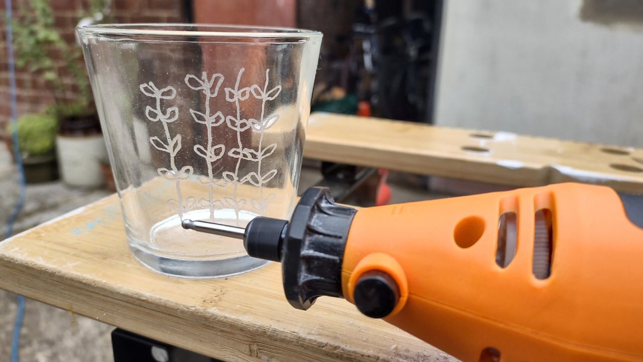 An orange rotary multi tool being used to engrave a glass with a delicate pattern